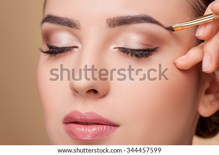 Close up of beautiful face of young woman getting make-up. The artist is applying eyeshadow on her eyebrow with brush. The lady closed eyes with relaxation Royalty-Free Stock Photo #344457599