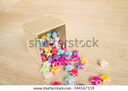 colorful of paper fold christmas stars spilling out from the paper box to wood surface