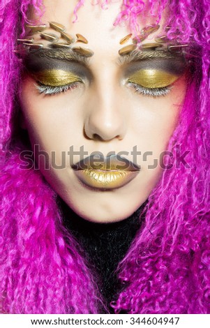 Closeup portrait of one beautiful wild young woman with bright golden animal monkey makeup with thorns on face in fur violet wig in studio, vertical picture