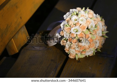 Photo closeup front view ball-shaped elegant wedding bouquet of fresh pastel pink white roses flowers with ribbons for bridal ceremony on wooden bench on dark timber background, horizontal picture 