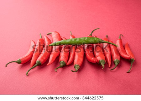Depicting uniqueness and against stream concept using fresh red and green chillies on colourful background