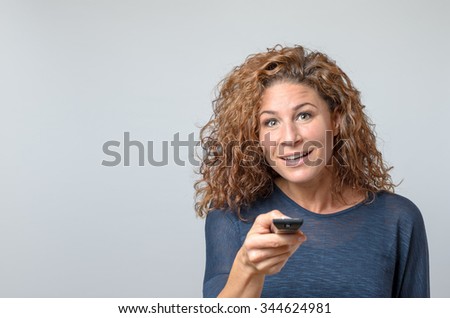 Close up Middle Aged Woman in Casual Pullover Holding Remote Control While Looking at the Camera, Isolated on Gray Wall Background.