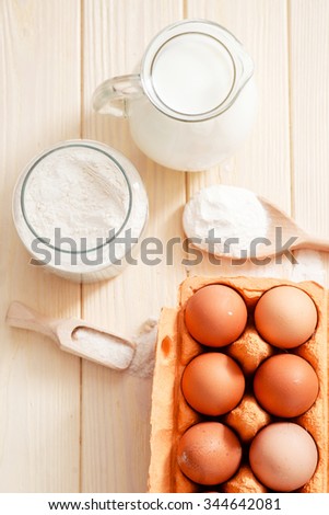the ingredients for the dough , eggs , milk, butter , salt and flour on a wooden background