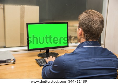 Young office male worker sitting at his desk working at computer, seen from the back. Chromakey PC monitor
