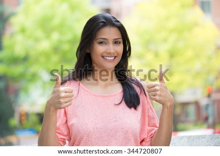 Closeup portrait of young pretty woman in pink shirt with two thumbs up sign gesture, isolated outdoors background. Positive emotion facial expression feelings, signs and symbols, body language Royalty-Free Stock Photo #344720807