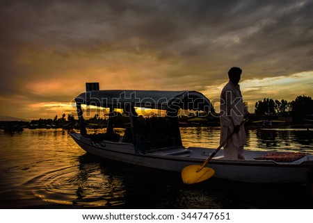 The silhouette of a boat glides along the surface of Dal Lake during sunset with Srinagar Fort in the background in Kashmir, India