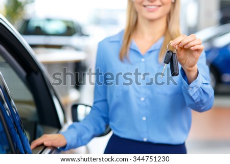 Your path to dreams. Selective focus of keys in hands of professional female sale assistant giving them to the customer and standing near the car in auto show