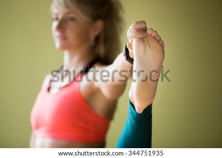 Sporty beautiful blond young woman in sportswear working out indoors, doing Utthita Hasta Padangustasana, Extended Hand To Big Toe yoga posture, close up, focus on foot