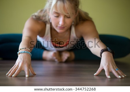 Sporty beautiful blond young woman in sportswear working out indoors, doing Butterfly Pose with closed eyes, sitting in Purna Titli or Baddha Konasana Posture, full length, close-up, focus on hands Royalty-Free Stock Photo #344752268