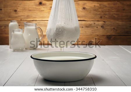 Cooking homemade cottage cheese on a wooden background. Dark rustic atmosphere. Cottage cheese in cheesecloth flows into the emulsion white dish on a white wooden table Royalty-Free Stock Photo #344758310