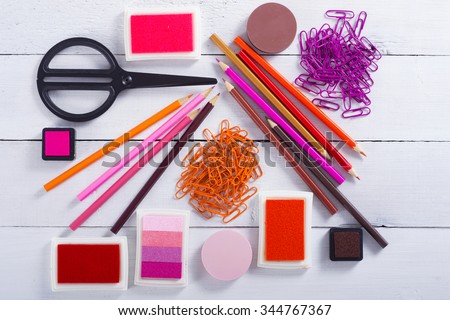 red, pink, purple color pencils and paper clips, ink pads on white wooden table background