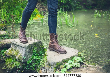 The feet of a young person trekking across stepping stones in a small pond Royalty-Free Stock Photo #344777630