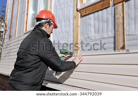 A worker installs panels beige siding on the facade of the house Royalty-Free Stock Photo #344792039