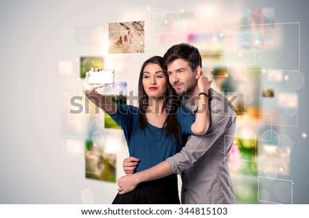 Collecting memories concept with photos in backbround and a happy young couple in love taking selfie with a mobile phone