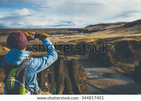 Back view of woman wearing winter clothes taking pictures of canyon in Iceland.