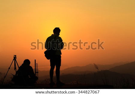 Silhouette of male traveler when he is taking photograph on mountain at sunrise.