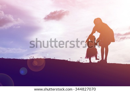 Silhouettes of mother and little daughter walking at sunset