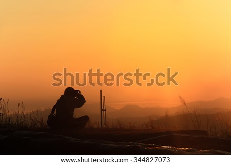 Silhouette of traveler when he is taking photograph on mountain at sunrise.