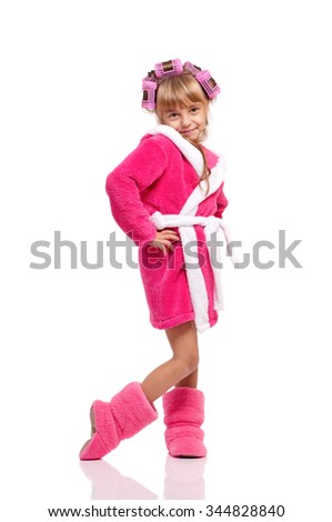 Full length portrait of pretty little girl in pink bathrobe with curlers on her head isolated on white background
