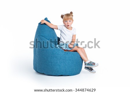 Creative photo of cute little girl isolated on white background. Surprised girl sitting on big frameless chair