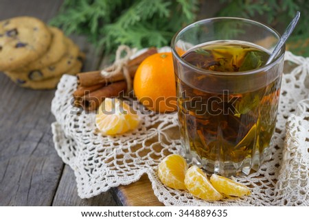 Christmas (New Year) composition. Glass cup of tea with mint, tangerine slices, cinnamon sticks, chocolate chip cookies and thuja branches on wooden background