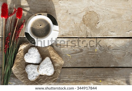 Heart shaped cookies (powdered sugar), cup of coffee, decoration (red flowers) on old wooden table. sunny morning.  Christmas breakfast or Valentine's Day Breakfast. Toned image