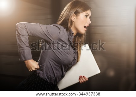 Stressed businesswoman running with laptop. Dark background.