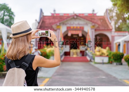 Tourism concept. Young woman with hat taking photo on smartphone while walking by the chinese town.