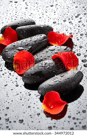 Spa stones with rose petals on black background