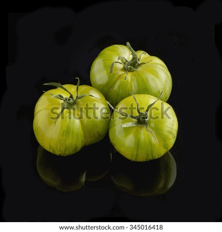 Three fresh whole green tiger tomatoes on a black background with reflection below