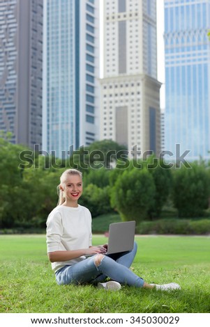 girl sitting on the grass with a laptop on the background of skyscrapers