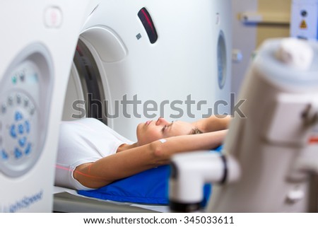 Pretty, young woman goiing through a Computerized Axial Tomography (CAT) Scan medical test/examination in a modern hospital (color toned image; shallow DOF) Royalty-Free Stock Photo #345033611