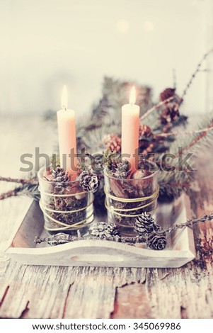 Still life photo of a Christmas candles burning bright with pine cones on rustic wooden background