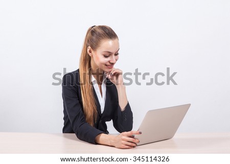 modern young business woman in a business suit on a white background minimalist office sits at a table in front of a laptop.