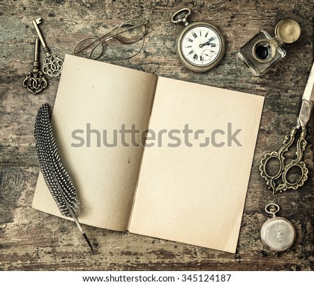 Open book and vintage office supplies on wooden table. Feather pen, inkwell, keys on textured background. Retro style toned 
