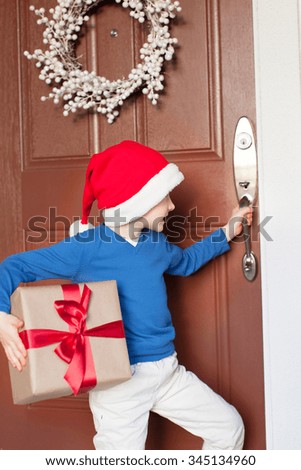 smiling little boy wearing santa's hat and holding wrapped christmas gift pretending to be an elf going home