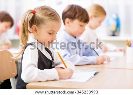 Collective work. Little pupils are all busy writing in their copybooks. Royalty-Free Stock Photo #345233993