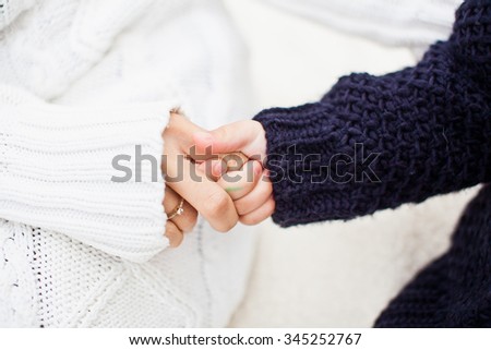 Mother holding her daughter hand. Daughter holding mom's finger. Both in warm and cozy sweaters. Daughter in blue or black sweater and mother in white sweater. Conceptual photo of diversity and family Royalty-Free Stock Photo #345252767