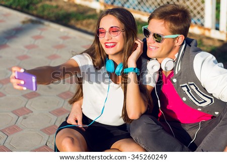 Lifestyle summer image of stylish beautiful  couple in love  making self portrait, having fun, enjoying time together, urban city background, hipster casual spring outfit , bright summer colors.