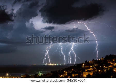 Massive cloud to ground lightning bolts hitting the horizon of city lights