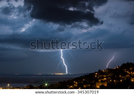 Massive cloud to ground lightning bolts hitting the horizon of city lights