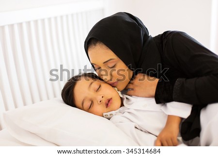 caring muslim mother kissing baby boy while he is asleep
