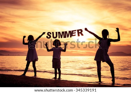 Happy children playing on the beach at the sunset time. Children hold in the hands  inscription "Summer"