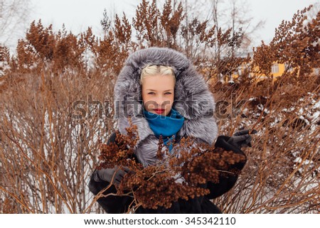 Blond girl with red lips in fur coat outdoors.