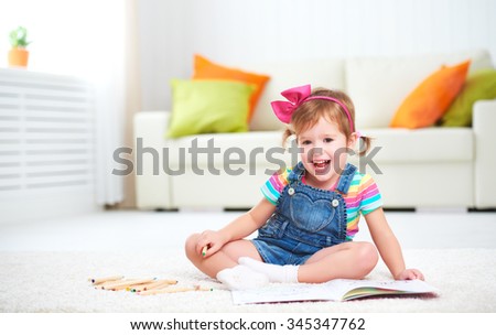 happy child girl drawing with colored pencils lying on the floor in the nursery