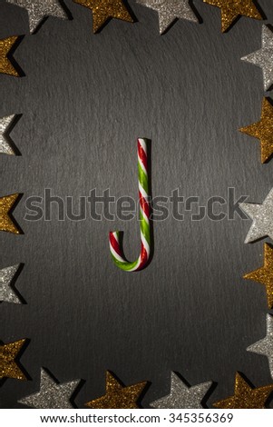 Red green striped candy cane on slate background with frame of golden and silver stars, Christmas decoration.