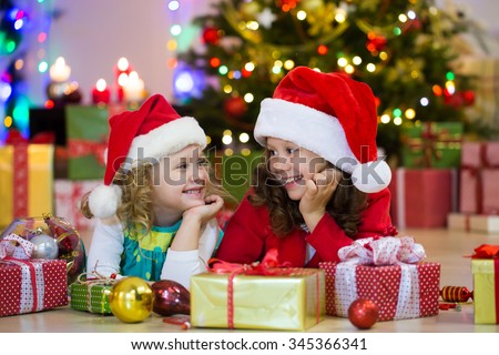 Two little girls in the Santa hat with the Christmas gift under the tree