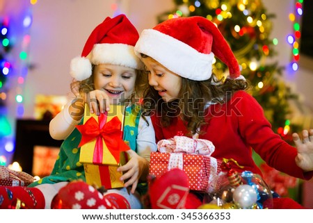 
Two little girls in the Santa hat open Christmas present under the Christmas tree