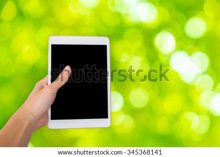 Hands are holding touch screen White Tablet Computer on green glitter sparkle defocused rays lights bokeh abstract background.