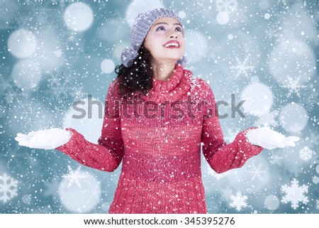 Portrait of cheerful indian woman wearing warm clothes while playing snow with bokeh background